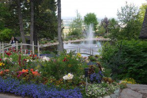 beautiful garden scene depicting a bridge spanning a pond surrounded by flowers with mountains in the background