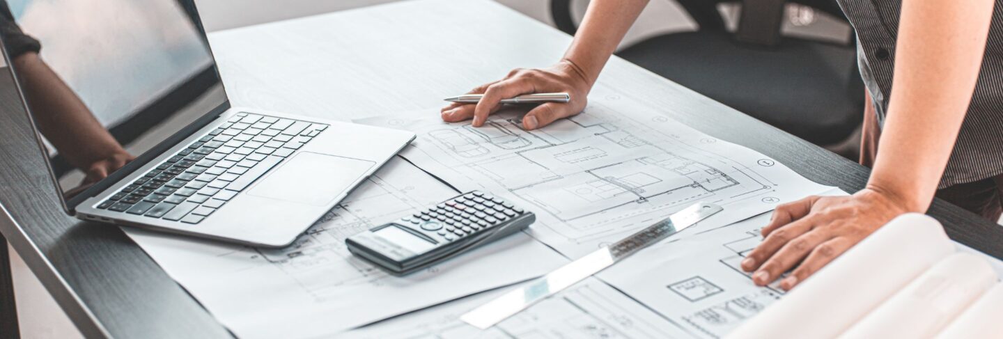 a person leans on a table with a laptop and blueprints