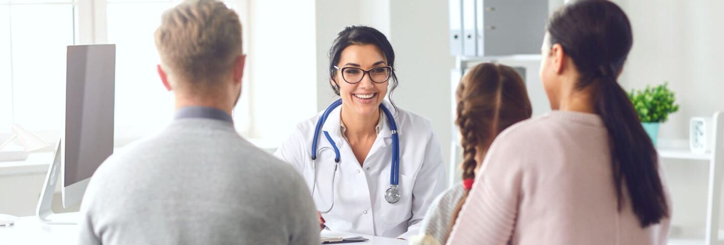 a doctor smiling at a family sitting in a doctor's office