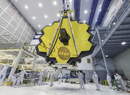 james webb space telescope being hoisted by a crane surrounded by technicians